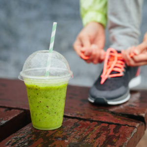 Green post-exercise protein shake and woman tying shoe