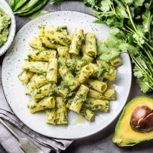 pesto pasta on a plate with avocado and herbs