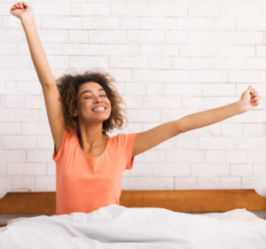 Lazy morning after a good night sleep. African-american woman stretching, sitting on bed